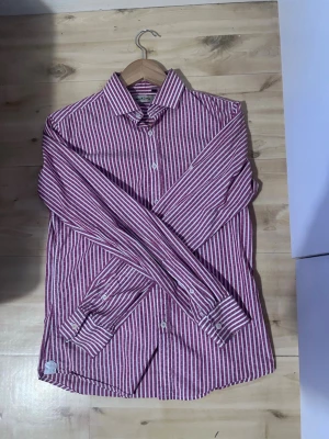Randig skjorta från Martins - Snygg skjorta från Martins i röd och vit randigt mönster. Skjortan har klassisk krage, långa ärmar och knäppning framtill. Perfekt för dig som vill sticka ut lite extra med en färgglad look.