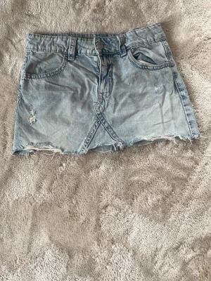  jeanskjol 💕 - Cool ljusblå jeanskjol med rå och fransig nederkant, klassiska fickor fram och bak samt broderade detaljer på bakfickorna. Kjolen har knapp och dragkedja framtill och är perfekt för en avslappnad stil. Säg till om du vill diskutera pris 💕
