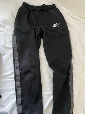 Nike Air svart loungewear set - Nike Air loungewear set i svart med grå detaljer. Setet består av en sweatshirt med halv dragkedja och stor logga på bröstet samt matchande byxor med sidofickor och logga på benet. Perfekt för chill dagar hemma eller när du vill vara bekväm.
