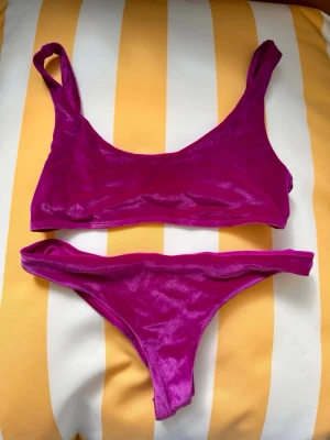Lila bikini i sammet storlek S - Snygg lila bikini med sportig topp och klassiska bikinitrosor. Materialet har en glansig finish som ger en lyxig känsla. Perfekt för strandhäng eller poolparty. Enkel och stilren design utan extra detaljer. Storlek S i båda.
