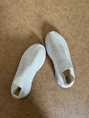 Vita slip-on sneakers strl 39 - Säljer ett par vita slip-on sneakers i stickad mesh med elastisk ovandel och ribbad kant. Skorna har en chunky sula och modern design utan snörning, vilket gör dem enkla att ta på och av. Perfekta för en clean och sportig look.