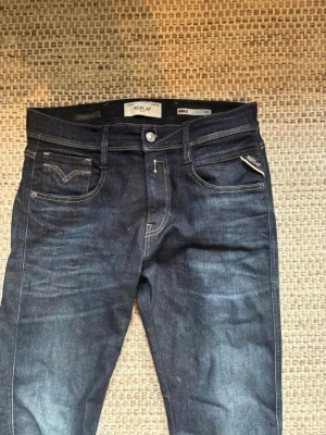 Mörkblå Replay jeans med stretch - Snygga mörkblå jeans från Replay med klassisk femficksmodell och guldfärgade sömmar. Jeansen har en slim fit passform och är tillverkade i stretchigt denimtyg för extra komfort. Perfekta för dig som gillar en modern och stilren look.