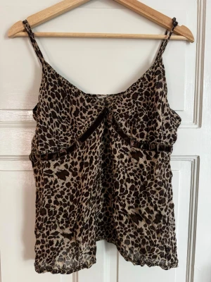 Leopardmönstrad topp med pärlor - Snygg leopardmönstrad linnetopp med tunna axelband och dekorativa pärlor längs kanten. Toppen har bruna och beiga toner. Perfekt för dig som vill sticka ut lite extra. Den är använd några gånger men k ett bra skick. Lappen sitter ej kvar så jag vet inte vart den kommer ifrån. 💕