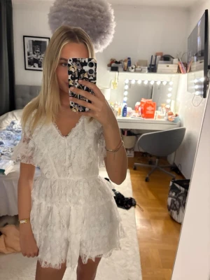 14+ lace dress - Säljer en superfin vit kortklänning med spets och volangdetaljer. Klänningen har v-ringning, korta ärmar. Från ginas studentklänning kollektion, helt ny med prislapp! Köpt för 400 säljer för 300