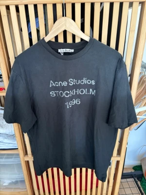 Svart Acne Studios t-shirt - Cool svart t-shirt från Acne Studios med trycket 'Acne Studios STOCKHOLM 1996' på bröstet. Klassisk rund hals och korta ärmar. Perfekt basplagg med street vibe och enkel stil. Tillverkad i mjuk bomull för skön känsla.Storlek L och i oanvänt skick. 