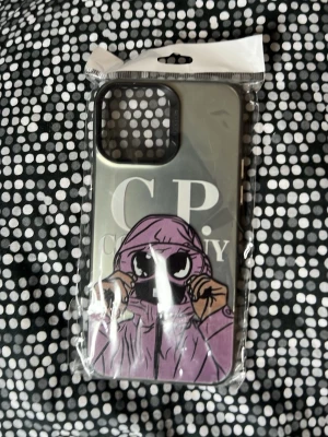 Mobilskal med CP Company-motiv - Snyggt mobilskal med CP Company-tryck och en tecknad figur i lila hoodie på baksidan. Skalet är genomskinligt med svart ram runt kameran och har en cool streetwear-vibe. Tillverkat i tålig plast som skyddar mobilen mot repor och stötar.
