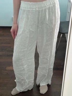 Vita vida linnebyxor - Säljer ett par vita linnebyxor med avslappnad passform och resår i midjan. Byxorna är luftiga och har raka ben, perfekta för en chill och bekväm stil. Materialet är tunt linne som ger en skön känsla. Inga fickor eller synliga detaljer. 100% linne.