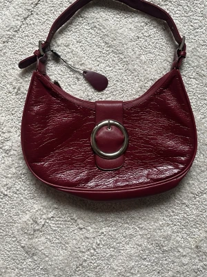 vinröd hoboväska - sååå snygg hobo väska med silver detaljer. köpt på en marknad utomlands och aldrig använd. säljaren sa att det är skinn men det skulle kunna vara nån mix, är inte helt säker på materialet. ca 36cm bred så perfekt storlek!