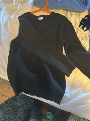 Svart stickad tröja från Kappahl - En enkel och stilren svart stickad tröja från Kappahl. Tröjan har rund halsringning, långa ärmar och ribbade muddar vid ärmslut och nederkant. Perfekt basplagg att matcha med olika outfits.