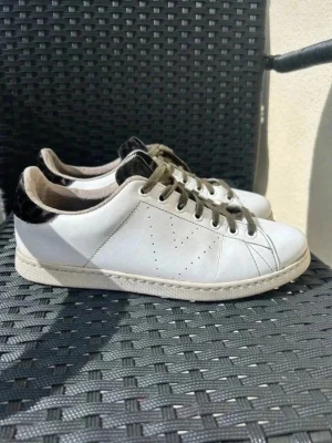 Vita Victoria sneakers med leopard detaljer - Säljer ett par vita sneakers från Victoria med snygga gröna leopard detaljer och mörkgröna snören. Skorna har klassisk låg profil, perforeringar på sidan och är tillverkade i läder. Perfekt för dig som gillar stilrena och tidlösa sneakers. Påminner väldigt mycket om de trendiga veja men enligt mig mycket snyggare. I storlek 41 men jag skulle säga att de passar runt 40. Skriv vid frågor💘 