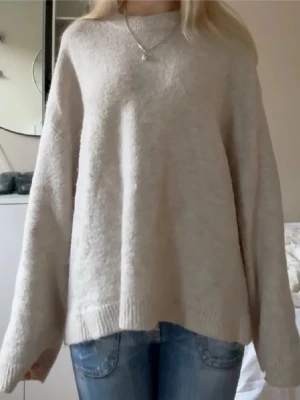 Beige stickad tröja med loose fit - Mysig beige stickad tröja med loose passform och långa ärmar. Tröjan har ribbade muddar vid ärmslut och nederkant, perfekt för att hålla värmen under kyliga dagar. Enkel och stilren design som är lätt att matcha med jeans eller andra favoritplagg.