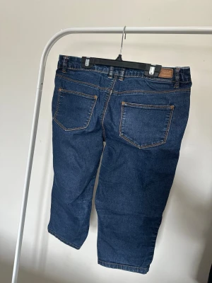 Blåa caprijeans med raka ben - Säljer ett par blåa caprijeans med raka ben och klassiska femficksdetaljer. Jeansen har kontrastsömmar och är tillverkade i denim med bomullskänsla. Perfekt för dig som vill ha ett avslappnat och snyggt jeansplagg.
