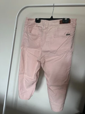Ljusrosa caprijeans - Säljer ett par ljusrosa caprijeans med klassisk femficksdesign och knappstängning. 