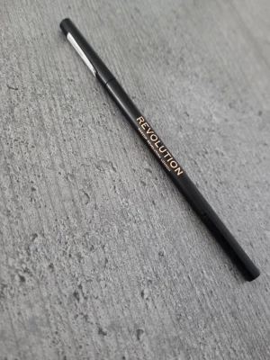 Revolution ögonbrynspenna medium brown - Snygg ögonbrynspenna från Revolution i färgen medium brown. Pennan har en smal och stilren svart design med guldtext. Perfekt för att fylla i och forma brynen med precision. Materialet är plast och pennan är enkel att använda.