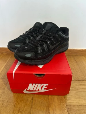 Nike svart p6000 - Snygga helsvarta Nike sneakers med mesh- och syntetpaneler, reflekterande detaljer på snörningen och klassisk swoosh på sidan. Skorna har en chunky sula och sportig vibe, perfekta för dig som gillar streetwear och vill ha något stilrent till vardags.