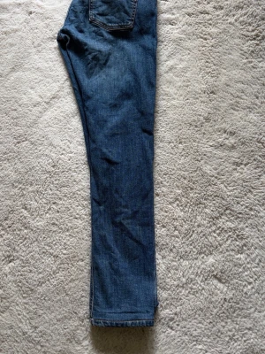 Nudie jeans W30L30 - Säljer ett par blå jeans med rak passform och klassiska bakfickor. Jeansen har en tidlös look och är gjorda i denim, perfekt för dig som gillar enkel och stilren design.