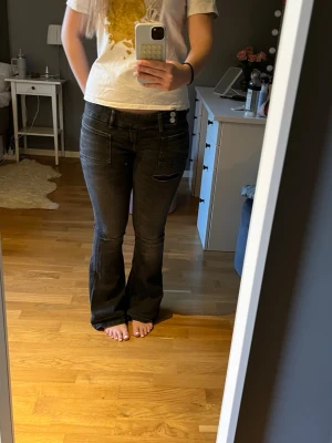 Svarta bootcut jeans med dubbla knappar - Säljer ett par svarta bootcut jeans med dubbla knappar i midjan och snygga fickdetaljer framtill. Jeansen har en klassisk femficksdesign och är tillverkade i ett stretchigt denim-material som sitter bekvämt. Perfekta för dig som gillar en cool och avslappnad stil.