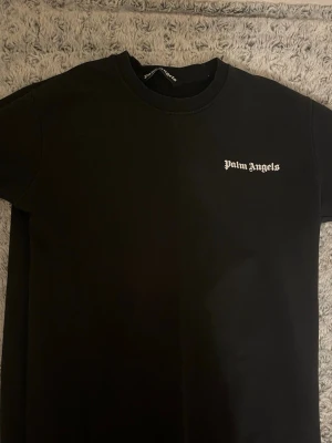 Palm angels tröja priset kan diskuteras! - Svart tröja från Palm Angels med vit logga på bröstet och stort tryck på ryggen med städer som Los Angeles, Paris, Hong Kong, Tokyo och Shanghai. Klassisk rund hals och korta ärmar. Materialet är mjuk bomull och passformen är normal. Passar även som M