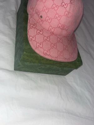 Rosa Gucci keps med monogram - Säljer en rosa keps från Gucci med det klassiska GG-monogrammet över hela kepsen. Kepsen har böjd skärm och är tillverkad i ett tygmaterial som ger en exklusiv känsla. Perfekt för dig som vill sticka ut med en ikonisk accessoar.
