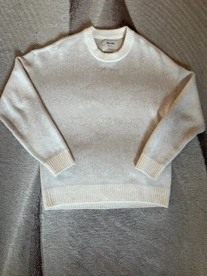 Beige stickad tröja från Hollister  - Snygg beige stickad tröja från Hollister med rund halsringning och ribbade muddar vid ärmslut och nederkant. Tröjan har en klassisk rak passform och är tillverkad i ett mjukt material som passar perfekt för kyligare dagar. Perfekt för layering. Passar XS och S.