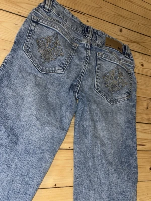 Blå bootcut jeans med broderi - Snygga ljusblå bootcut jeans med slitna benslut och broderade detaljer på bakfickorna. Jeansen är kortare än vanligt då jag klippt upp dom. Säljer då dom blev för korta.. innebenslägnd 64cm ytterbenslägnd ca 86cm