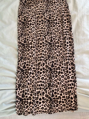 Långkjol med leopardmönster - Säljer en långkjol med coolt leopardmönster i beige och svart. Kjolen har rak passform och är perfekt för dig som vill sticka ut. Materialet känns mjukt och bekvämt, troligtvis polyester. Passar dig som gillar djurmönster och vill ha en trendig look.