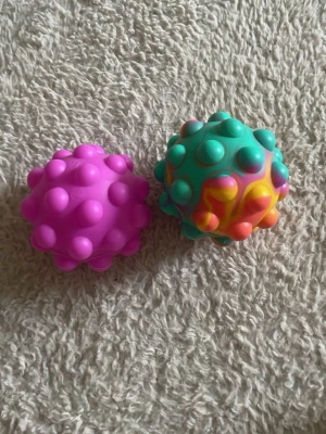 2 pop it bollar - 2 pop it bollar, 1 multi färgad och 1 rosa. Dem studsar men funkar också som pop its, väldigt roliga. 