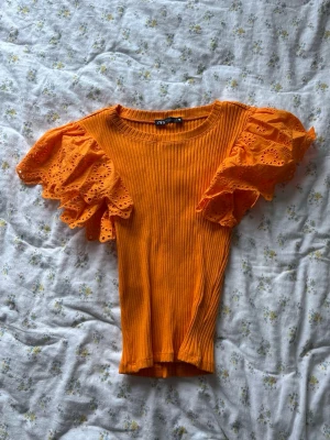 Orange ribbad topp med volangärmar från Zara - Säljer en orange ribbad topp från Zara med stora volangärmar i spets och broderade detaljer. 