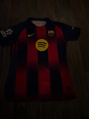 FC Barcelona matchtröja Nike - Snygg FC Barcelona matchtröja i rött och marinblått med gula detaljer. Tröjan har klubbmärke, Nike-logga och Spotify som sponsor framtill. På ryggen står det Lamine Yamal och nummer 10 i gult. Perfekt för dig som älskar fotboll och Barca!