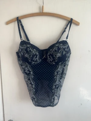 Mörkblå spetsbody med blommönster - Snygg mörkblå body med vita prickar och detaljerad spets i blommönster. Justerbara axelband och vadderade kupor för extra stöd. Transparent mesh på sidorna. Köpt på vinted och står tyvärr inget märke i. Storlek Large (tyvärr för stor för mig) 💗