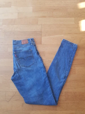 Blå Levi's skinny jeans - Säljer ett par klassiska blå skinny jeans från Levi's med femficksdesign och ikonisk röd Levi's-tag på bakfickan. Jeansen har hög midja och är tillverkade i slitstark denim. Perfekt för dig som gillar en tidlös och cool look.