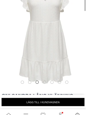 Vit kortklänning med volangärm - Söt vit kortklänning med v-ringning och volangärmar. Klänningen har broderade detaljer och en volangkant nedtill som ger en romantisk känsla. Perfekt för sommarens alla tillfällen. Tillverkad i lätt bomullstyg som andas.