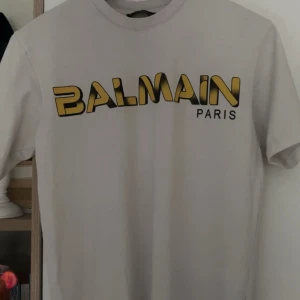 Balmain T-shirt - Vit t-shirt från Balmain Paris med stort, coolt gult och svart logotryck på bröstet. Klassisk rund hals och korta armar. Perfekt för dig som gillar streetstyle och vill sticka ut med ett lyxigt märke. Själv är jag väldigt nöjd med t-shirten. Tröjan är m storlek men passar även s priset kan även diskuteras. Hör av er.