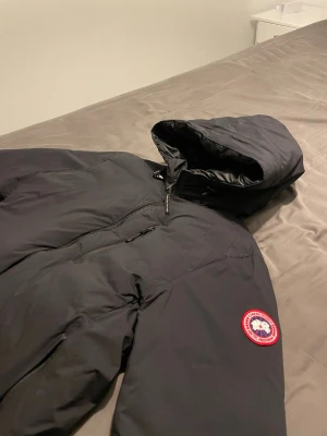 Canada Goose Lodge Hoody - Säljer en äkta Canada Goose Lodge Hoody i svart. Perfekt lättviktsdunjacka som funkar både som ytterplagg och som mellanlager. Skick: Använd i befintligt skick. Finns tecken på användning:  * Mindre skada/hål vid ärmen (se bild)  I övrigt bra skick 
