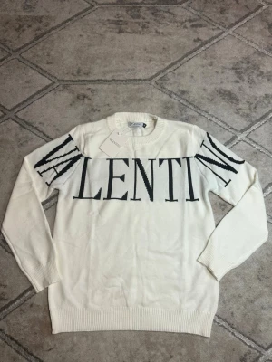 Vit stickad tröja från Valentino - Valentino Stickad Tröja - Vit/Svart Stickad tröja från Valentino i vit bas med svart logotyp över bröst och ärmar. Plagget är tillverkat i en finmaskig stickning som passar för sena sommarkvällar. 🌘🌆                                                                  OBS!: finns i både storlek S och M.