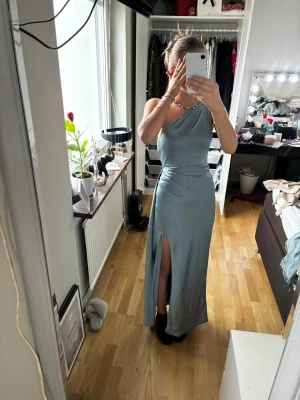 Perfekt balklänning Ljusblå långklänning med slits - Snygg ljusblå långklänning med oneshoulder och smala axelband. Klänningen har en elegant slits framtill och är figurnära med en mjuk, glansig finish. Perfekt för dig som vill sticka ut med en stilren look.