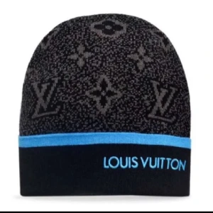 Louis Vuitton svart mössa med blå kant - Cool svart mössa från Louis Vuitton med klassiskt monogrammönster i grått och en blå kant med broderad logotyp. Perfekt för dig som vill ha en exklusiv och trendig accessoar. Materialet ser ut att vara mjukt och stretchigt.
