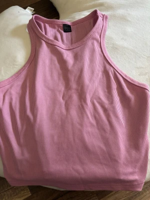 Rosa ribbad linnetopp från SHEIN - Säljer en rosa och en svart ribbad linnetopp från SHEIN med hög halsringning och ärmlös design. Toppen har en normal passform och är tillverkad i ett mjukt syntetmaterial som är perfekt för varma dagar. Enkel och stilren look som är lätt att matcha.