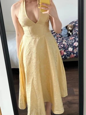 Ljusgul klänning från Cider - Helt oanvänd! Lapp sitter kvar!                      Utpsrungspris 650kr —> mitt pris 500 kr.    Ljusgul långklänning med halterneck och v-ringning. Klänningen har ett subtilt blommigt mönster i tyget och knyt i nacken..