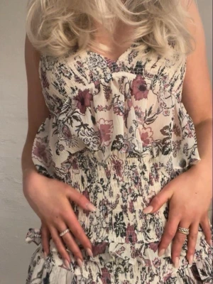 Zara Blommig linnetopp med volang  - Supersöt blommig linnetopp med volang och smala axelband. Toppen har en ljus bas med lila och rosa blommor, v-ringning och en flowy passform. Perfekt för varma dagar och enkel att styla med jeans eller kjol.