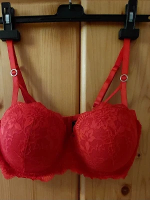 Röd Bh Bodyflirt 90D - Säljer en snygg röd Bh från Bodyflirt med blommig spets och dubbla axelband. Bh har vadderade kupor. Oanvända 