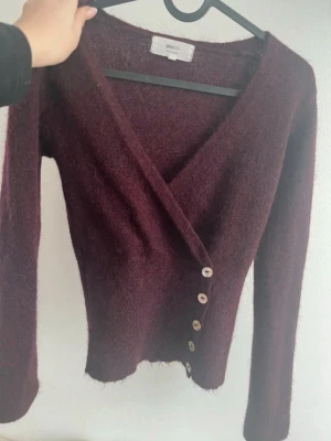 Vinröd omlottkofta från Gina Tricot - Avänd 1 gång (som ny) mysig vinröd omlottkofta i alpackablandning från Gina Tricot. Koftan har långa ärmar, v-ringning och stängs med sex silvriga knappar framtill. Perfekt för lager på lager och ger en trendig look.