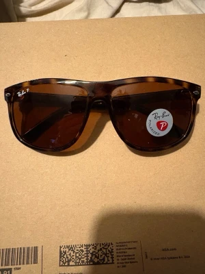 Ray-Ban bruna solglasögon RB4147 - Snygga Ray-Ban RB4147 solglasögon med brunmelerad båge och bruna polariserade glas. Klassisk och tidlös modell som passar till många stilar. Märket syns tydligt på linsen och insidan av skalmen. Perfekta för soliga dagar!