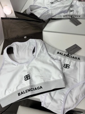 Vit baddräkt - Snygg vit baddräkt med sportig design. Den har svarta logotyper och breda resårband. Materialet är stretchigt och bekvämt, perfekt för en modern look 