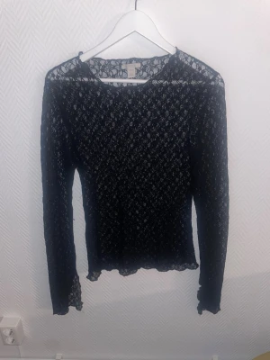 Svart spetsblus från Amisu - Säljer en svart långärmad spetsblus från Amisu i storlek L. Blusen är genombruten med ett elegant spetsmönster och har en figurnära passform. Perfekt för dig som vill ha en snygg och trendig topp med det lilla extra.