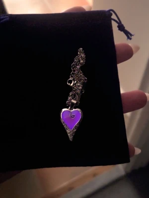 Halsband med färgskiftande hjärthänge - Unikt handgjort halsband med ett hjärtformat hänge som skiftar färg mellan rosa och lila beroende på ljus. Hänget har silverfärgad metallram med dekorativa snirkliga detaljer och en tunn kedja i rostfritt stål. Perfekt accessoar för dig som gillar personliga smycken med cool twist. Kedjan är 45 cm och hänget ca 2,5 cm. Både kedjan och hänget tål vatten & har en lång livslängd. Ljuseffekten aktiveras av vanligt dagsljus och håller i sig i flera timmar, upp till 12 timmar. 
