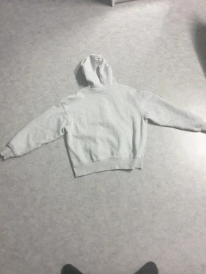 Ljusgrå zip hoodie - Ljusgrå hoodie med dragkedja framtill och snörning i huvan. Klassisk passform med ribbade muddar vid ärmar och midja. Perfekt för chill dagar eller när du vill ha en enkel och clean look.