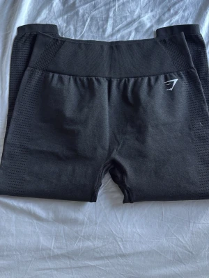 Svarta seamless tights Gymshark - Säljer ett par svarta seamless shorts från Gymshark med hög midja och stretchigt material. Shortsen har diskret logga framtill och ribbade detaljer i midjan och längs sidorna för extra komfort. Perfekta för gym och träning.