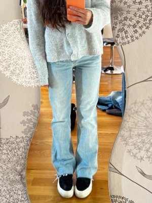Ljusblå bootcut jeans - Säljer ett par ljusblå bootcut jeans med råa kanter nertill. Jeansen har klassisk femficksdesign och hög midja. Perfekta för dig som gillar en avslappnad men trendig look. Midje: 36cm och innebenslängd: 74cm