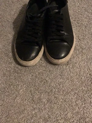 Svarta sneakers från Axel Arigato - Stilrena svarta sneakers från Axel Arigato med lågt skaft och vita sulor. Skorna är gjorda i slätt läder och har svarta skosnören. Perfekta för en clean och modern look.